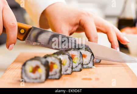 Coltello in mano taglia il rotolo closeup su una tavola di legno Foto Stock