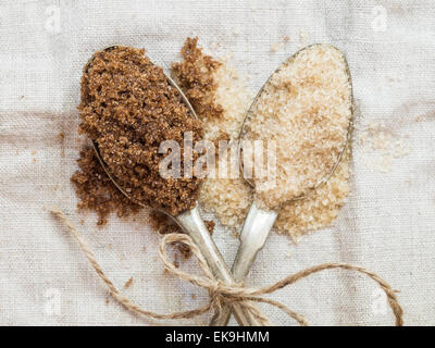 Foto orizzontale muscovado e demerara organica marrone zuccheri su due cucchiai di argento collocata su un rustico tovaglie di lino, vicino. Foto Stock