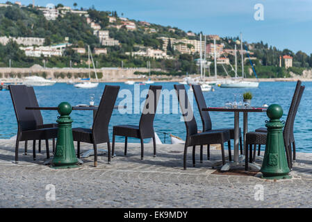 Una coppia di tavolini sul bordo del porto con barche in background Foto Stock