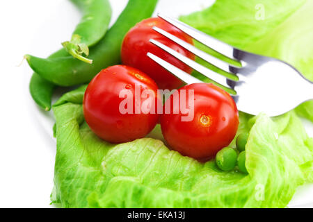 Pomodoro, piselli e lattuga con una forcella su una piastra isolata su bianco Foto Stock