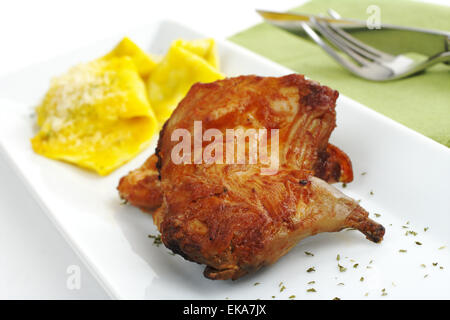 Piatto principale: Guinea la carne di maiale con ravioli su bianco piastra rettangolare con tavolo verde mat e posate in background Foto Stock