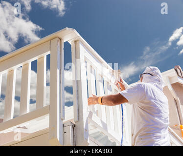 Pittore di casa indossando la protezione del viso verniciatura a spruzzo di un ponte di una casa. Foto Stock