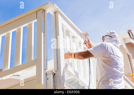 Pittore di casa indossando la protezione del viso verniciatura a spruzzo di un ponte di una casa. Foto Stock