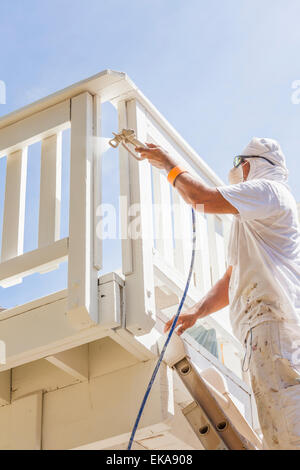 Pittore di casa indossando la protezione del viso verniciatura a spruzzo di un ponte di una casa. Foto Stock