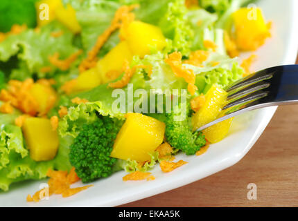 Fresco e leggero broccoli-mango-Insalata di carote sulla piastra bianca con un pezzo di mango sulla forcella (molto leggera profondità di campo) Foto Stock