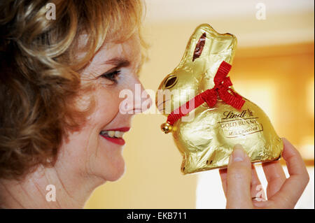 Donna matura guardando avanti a mangiare il cioccolato Lindt bunny o coniglio a Pasqua Foto Stock