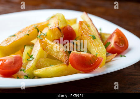 Patate fritte con pomodorini in bianco piatto sulla tavola di legno Foto Stock