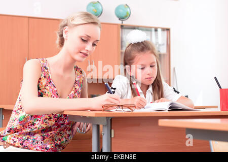 Insegnante seduta vicino allievo Foto Stock