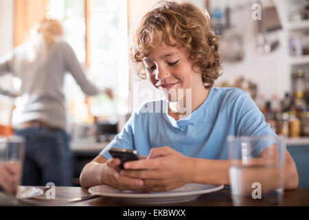 Ragazzo adolescente utilizza lo smartphone al tavolo da pranzo Foto Stock