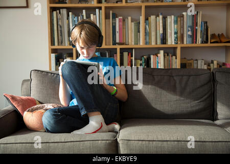 Ragazzo ascoltando musica su cuffie e con tavoletta digitale Foto Stock