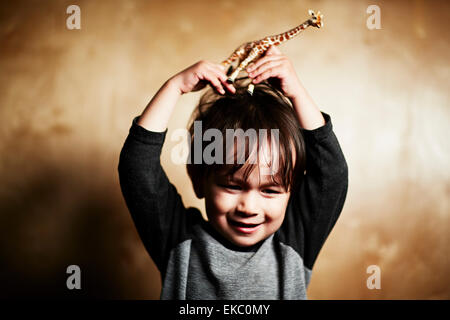 Ritratto di cute toddler maschio holding toy giraffa sulla sua testa Foto Stock