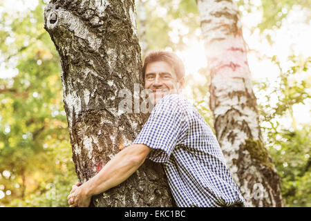 Uomo maturo abbracciando albero in giardino Foto Stock