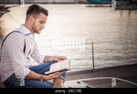 Giovane uomo la lettura su yacht, Cagliari, Sardegna, Italia Foto Stock