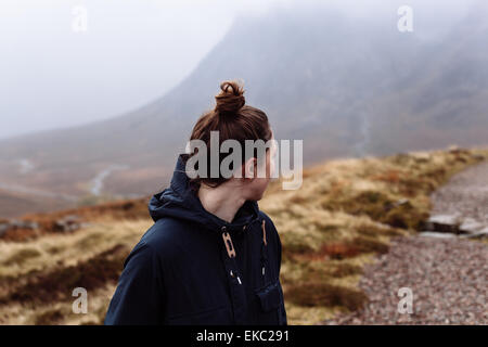 Donna che guarda oltre la spalla verso le montagne Foto Stock