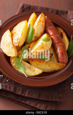 Patate al forno cunei e salsiccia a piastra sul brown tavolo rustico Foto Stock