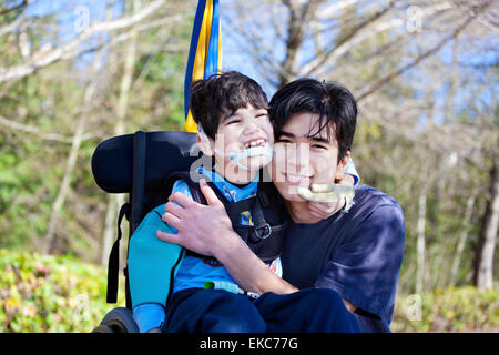 Little Boy disabili in carrozzella abbracciando il fratello maggiore all'aperto Foto Stock