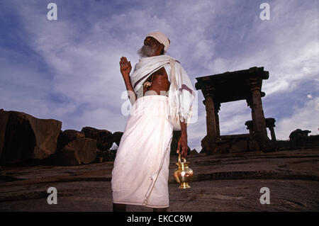 Un sacerdote Pujari o indù fa il gesto della mano rituale di Mudra tra i gruppi di santuari antichi che appartengono a entrambi, Pre-Vijayanagara e periodi di Vijayanagara situati sulla collina di Hemakuta nell'antico villaggio di Hampi annidato tra le rovine della città medievale di Vijayanagar nello stato di Karnataka in India Foto Stock