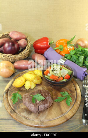 Arrosto bistecche di carne di struzzo con patate al forno e le verdure su una tavola di legno Foto Stock