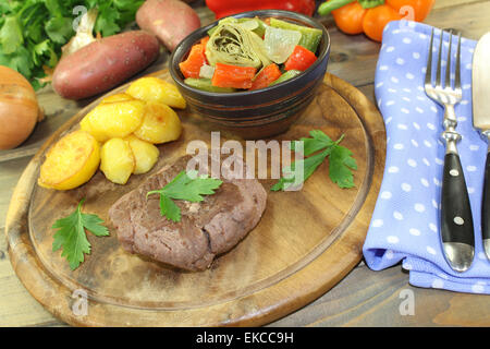 Arrosto bistecche di carne di struzzo con patate al forno e prezzemolo su una tavola di legno Foto Stock