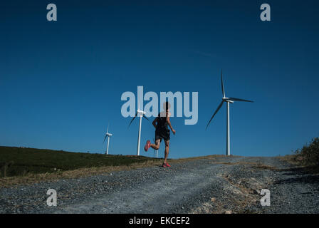 Metà uomo adulto jogging sulla strada, le turbine eoliche in distanza Foto Stock