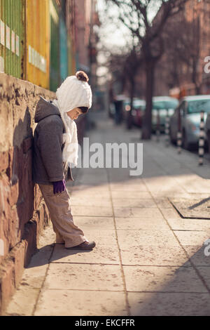 Ragazzo appoggiato contro una parete guardando verso il basso in corrispondenza di marciapiede Foto Stock