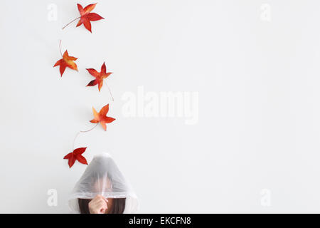 Autunno foglie cadere su una donna in un impermeabile Foto Stock