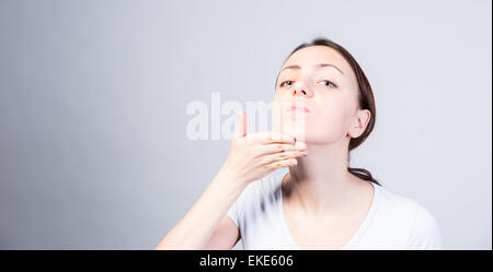 Giovane donna inclinando la testa mentre si solleva il suo mento e guardando la telecamera sul serio. Catturate in Studio su sfondo grigio Foto Stock