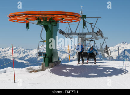 Due maschio sciatori scendere una seggiovia nel comprensorio sciistico svizzero di Verbier. Si sta usando un telefono cellulare. Foto Stock