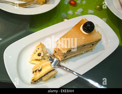 Piattino bianco con un delizioso pezzo di torta alla vaniglia e cioccolato sormontato da una ciliegia Foto Stock