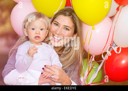 Ritratto di poco adorabile bambina festeggia il compleanno con la sua bella madre allegro, palloncini colorati decorazione Foto Stock