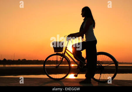 Stagliano donna con la bicicletta in corrispondenza del fiume Mekong waterfront al tramonto, Vientiane, Laos, sud-est asiatico Foto Stock