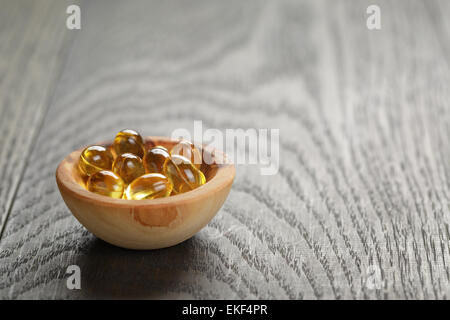 Olio di pesce capsule in ciotola di legno su un tavolo di legno Foto Stock