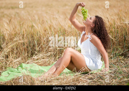 Donna perfetta mangiare uva nel campo di grano. Il Picnic. Foto Stock