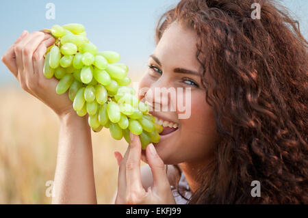 Donna perfetta mangiare uva nel campo di grano. Il Picnic. Foto Stock