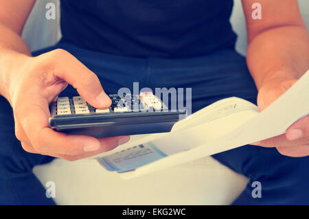 Primo piano di un giovane uomo di controllo una fattura, un bilancio o un libro paga con una calcolatrice, effetto filtrato Foto Stock