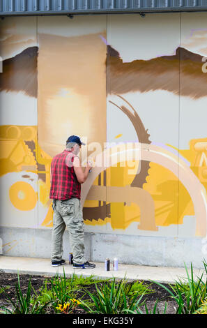 Graffiti artista che lavora su un grande murale sulla facciata del Fiume Margaret azienda lattiero-casearia parete in fabbrica in Australia Occidentale Foto Stock
