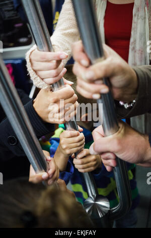 Molte mani tenendo allo stesso palo in un vagone della metropolitana Foto Stock