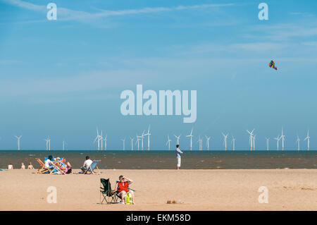 Famiglie rilassante e un uomo volare un aquilone a Skegness Beach con turbine eoliche in background Foto Stock