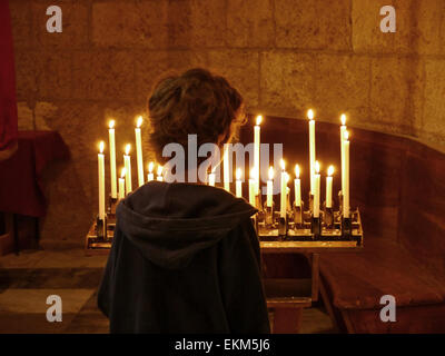 Un giovane ragazzo guardando alcune candele accese in una chiesa Foto Stock