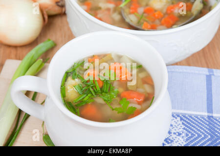 Fresca zuppa di verdure in bianco ciotola, erbe all'interno, grande scodella in background, argento bilanciere interno, vista aerea, Foto Stock