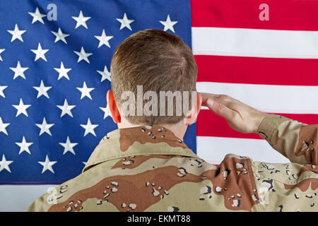 Close up immagine soldato maschio, torna alla fotocamera, salutando gli Stati Uniti d'America bandiera mentre in ambienti chiusi non indossano sentire l'ingranaggio. Foto Stock