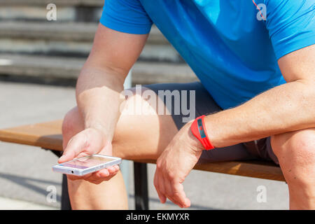 Uomo sportivo si siede su un banco di lavoro e verifica la sua idoneità risultati su uno smart phone. Foto Stock