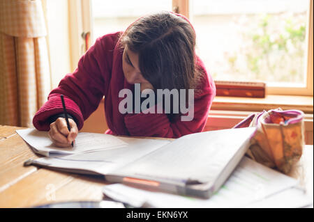 Adolescente di concentrare e studiando per gli esami come un livello in un ambiente di casa prendendo su tavolo da pranzo Foto Stock