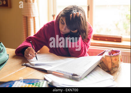 Adolescente di concentrare e studiando per gli esami come un livello in un ambiente di casa prendendo su tavolo da pranzo Foto Stock