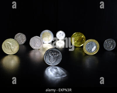 Monete da diverse valute riflessa su una superficie nera. Foto Stock