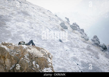 Un uomo, un escursionista in montagna, prendendo un resto giacenti su uno sperone di roccia al di sopra di una valle. Foto Stock