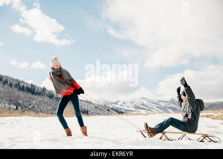 Una giovane ragazza tirando il suo fratello su una slitta attraverso la neve. Foto Stock