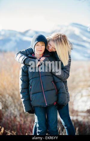 Un ragazzo in una camicia e cappellino essendo abbracciato da sua madre. Foto Stock