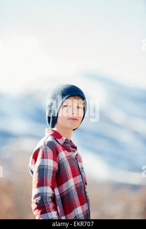 Un ragazzo con un cappellino e maglietta controllati in piedi in aperta campagna in inverno. Foto Stock