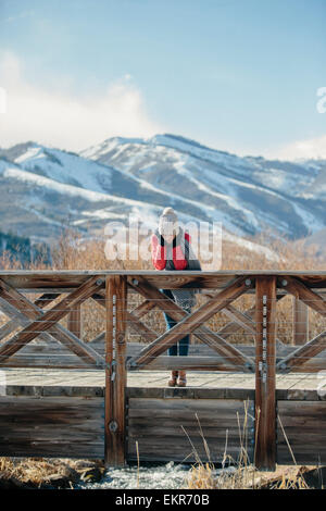 Una ragazza in una camicia rossa con un cappellino su appoggiata sopra la rotaia di un piccolo ponte pedonale. Foto Stock